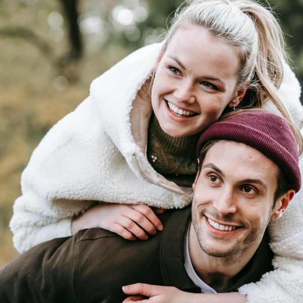 Person smiling and stretching outdoors in a park with green trees.